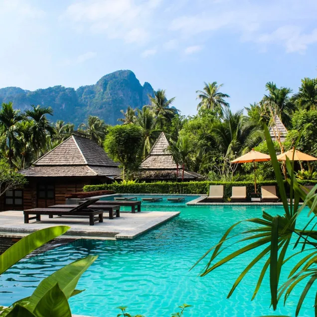Luxurious tropical resort with turquoise pool, thatched bungalows, and karst mountains.