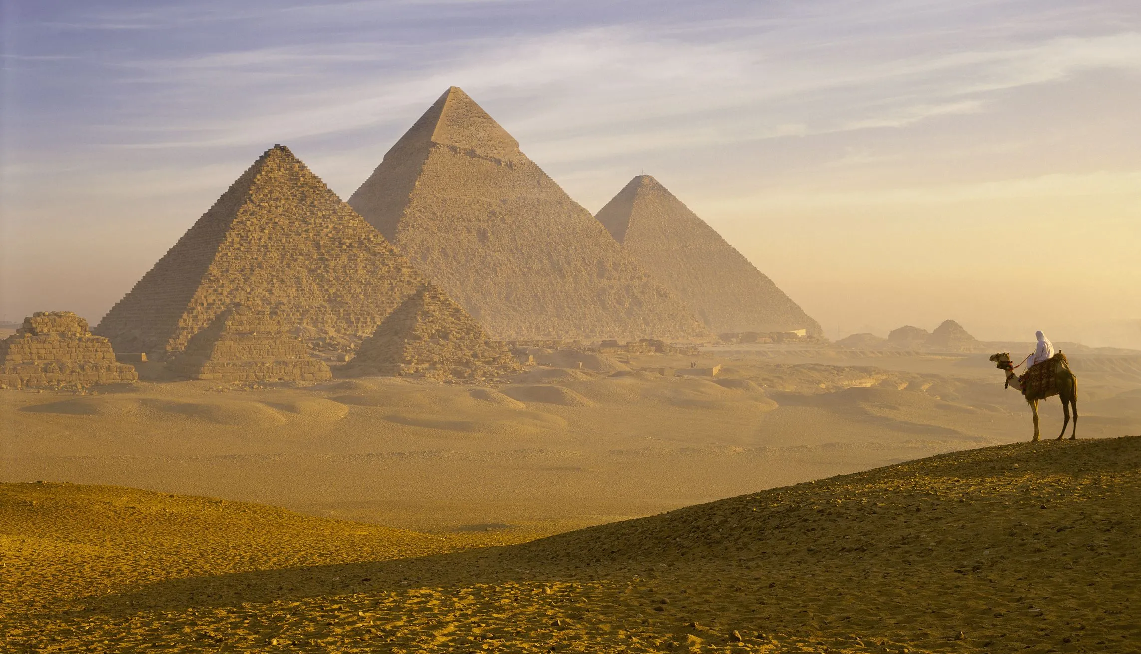 Majestic Pyramids of Giza at sunset over desert with camel rider.