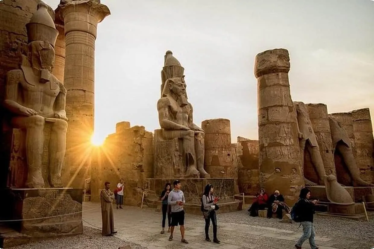 Colossal pharaoh statues and columns at Karnak Temple complex during sunset.
