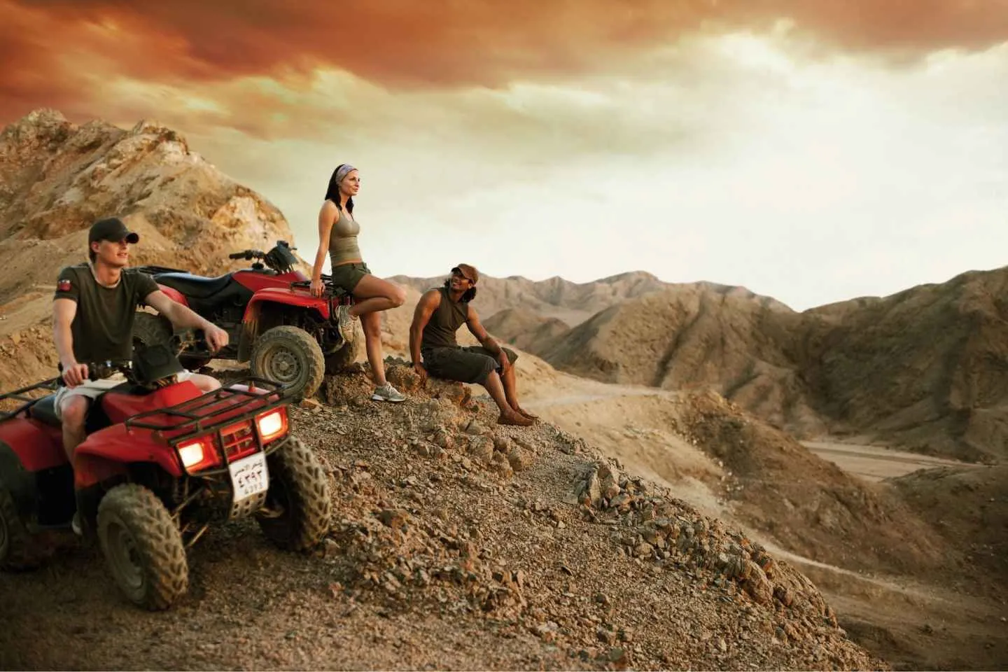 Three people resting with red quad bikes in rugged South Sinai desert mountains.