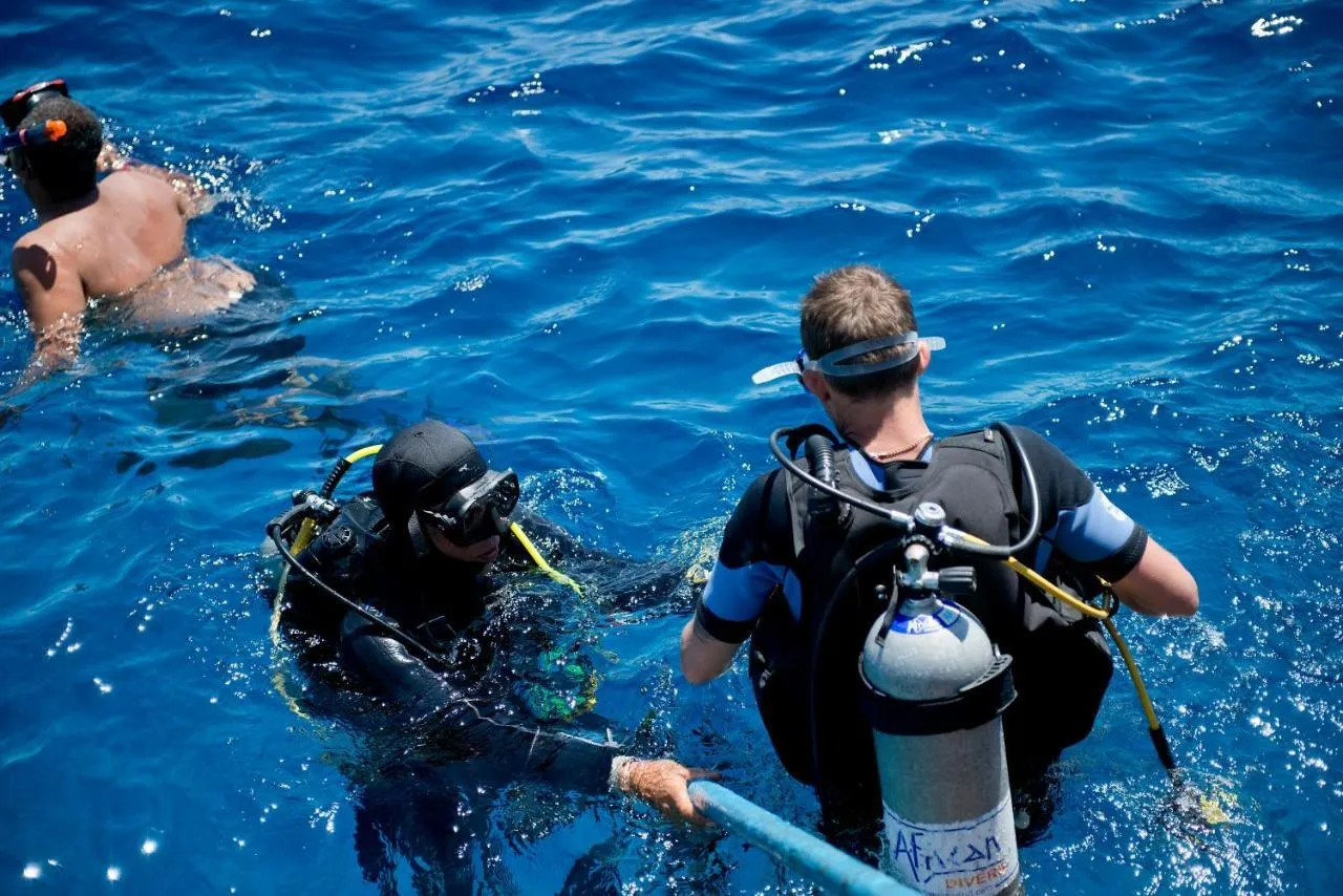 Scuba divers preparing for shore diving in deep blue, sunlit water, Sharm El Sheikh.