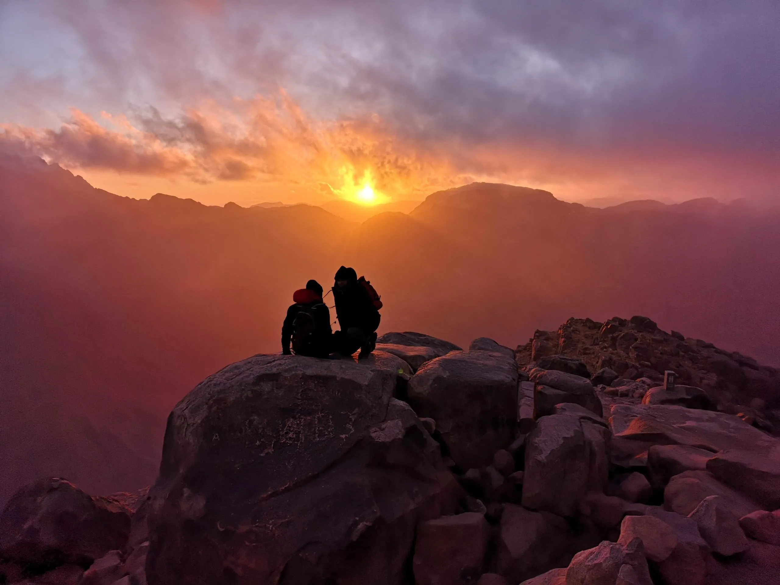 Sunrise over Sinai Desert from Mount Moses summit with two hikers.